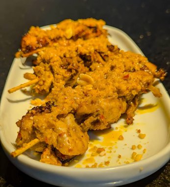 Fıstık sosuyla kaplanmış lezzetli ızgara tavuk şişleri parlak beyaz bir tabakta servis edilir..