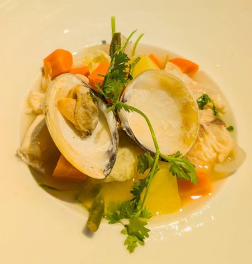 İçinde taze bitkilerle süslenmiş havuç, yeşil fasulye ve kabakla hafif bir çorba bulunan gurme bir deniz ürünleri tabağı..