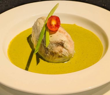 Canlı yeşil köri sosuyla servis edilen, kiraz domatesiyle süslenmiş ve köşegen olarak yerleştirilmiş taze soğan saplarıyla servis edilen yumuşak bir balık tabağı..