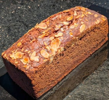 Üzerine kızarmış badem ekmekleri konmuş, parlak dokusunu ve koyu kahverengi rengini arttırmak için koyu bir yüzeyde sunulan zengin bir çikolatalı ekmek..