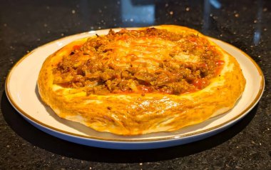 Kıyma, karamelli soğan ve erimiş peynirle kaplı taze pişmiş lezzetli bir hamur işi, altın kenarlı beyaz bir tabakta servis edilir..