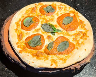 Erimiş peynir, domates sosu ve taze fesleğen yapraklarıyla kaplı, ahşap bir tahtanın üzerinde taze pişmiş Margherita pizzası servis edilir..