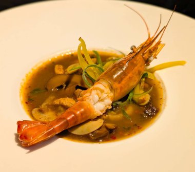 Mantarlı, jülyen dolmalık biberli ve soğanlı bir sebze çorbası üzerine koca bir karides içeren zarif bir deniz ürünleri sunumu..