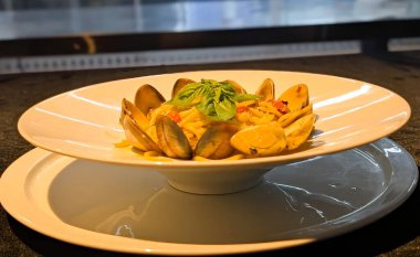 İstiridyeler, doğranmış domatesler, şifalı otlar ve taze fesleğenli yapraklarla servis edilmiş bir tabak spagetti. Zarif bir şekilde beyaz bir tabağa yerleştirilmiş..