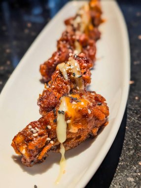 Zengin kırmızımsı kahverengi sosla kaplanmış, kremalı beyaz sosla kaplanmış ve üzerine siyah beyaz susam tohumları serpiştirilmiş tavuk kanatları..