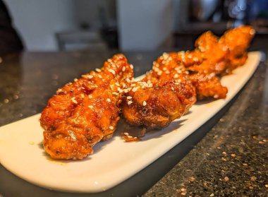 Zengin kırmızımsı kahverengi sosla kaplanmış, kremalı beyaz sosla kaplanmış ve üzerine siyah beyaz susam tohumları serpiştirilmiş tavuk kanatları..