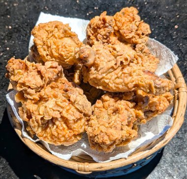 Çıtır çıtır tavuk kızartmalarıyla dolu bir sepet parlak doğal ışık altında çıtır çıtır ve sulu dokusunu sergiliyor..