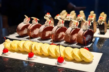 Krem şanti, kiraz ve beyaz çikolata parçalarıyla kaplı sarı ve kırmızı kadife İsviçre dürümleri de dahil olmak üzere çeşitli sarılmış pastalar..