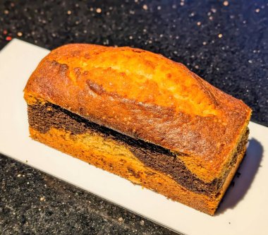 Vanilya ve çikolata hamuru karışımından oluşan klasik bir mermer ekmek keki. Nemli ve yumuşak bir kırıntıyla altın bir finale fırınlanmış..