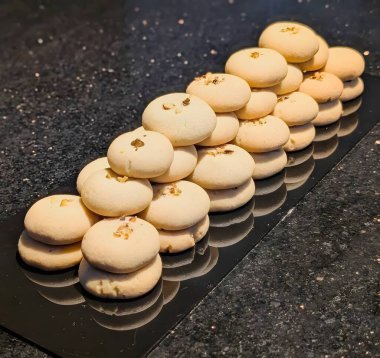 Bir yığın geleneksel Hint Nankhatai kurabiyesi üzerine doğranmış fındık, yansıtıcı siyah bir yüzeye yerleştirilmiş..