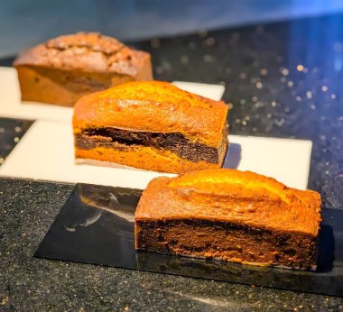 Zarif bir yansıtıcı yüzeyde, nemli kırıntılarını, tereyağlı dokusunu ve zengin vanilya tadını vurgulayan klasik pastanın sıcak altın dilimleri..