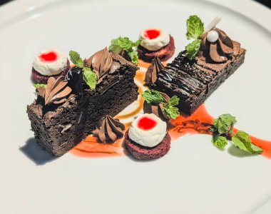 Krema ve nane ile kaplı zengin çikolatalı pasta dilimlerinin yanı sıra krem şantili ve şuruplu kırmızı kadife mermilerin yer aldığı zarif bir tatlı tabağı..