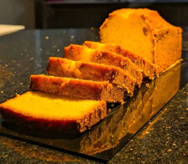 Zarif bir yansıtıcı yüzeyde, nemli kırıntılarını, tereyağlı dokusunu ve zengin vanilya tadını vurgulayan klasik pastanın sıcak altın dilimleri..