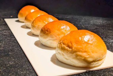 Beyaz dikdörtgen bir tepside düzgünce yerleştirilmiş, pırıl pırıl altın kaplamalı beş yeni pişmiş ekmek rulosu..