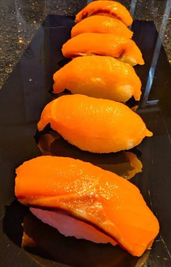 Altı sıra somon nigiri suşi dilimi. Parlayan portakal balığı dilimleri beyaz pirincin üzerinde. Parlak siyah bir tabakta güzelce sıralanmış..