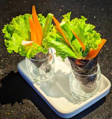 İki yosun kaplı sebze rulosu marul, havuç, salatalık ve turpla dolu, beyaz bir tepside cam bardaklarda sunuluyor..