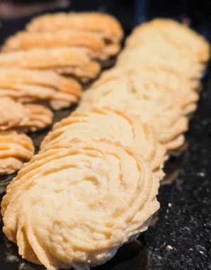 Derli toplu tereyağlı kurabiyeler, koyu bir yüzey üzerinde iki sıra halinde sergilenen kıvrımlı ve kıvrımlı dokular..