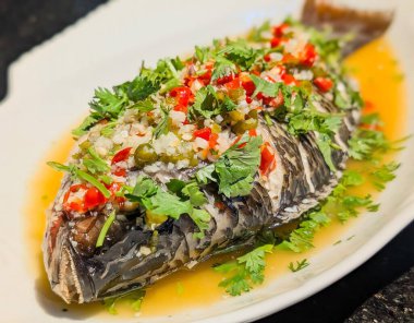 Açık kahverengi soslu tam pişmiş balık, doğranmış sarımsak, kırmızı ve yeşil biber, kapari ve taze kişniş ile süslenmiş..