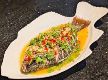 Açık kahverengi soslu tam pişmiş balık, doğranmış sarımsak, kırmızı ve yeşil biber, kapari ve taze kişniş ile süslenmiş..