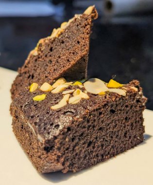 Dilimlenmiş badem ve doğranmış şam fıstığı ile süslenmiş, beyaz bir yüzeye istiflenmiş çikolatalı pasta dilimleri..