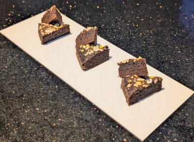 Dilimlenmiş badem ve doğranmış şam fıstığı ile süslenmiş, beyaz bir yüzeye istiflenmiş çikolatalı pasta dilimleri..