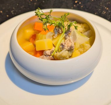 İçinde doğranmış havuç, patates, sarı kabak, karnabahar, soğan ve taze maydanozla süslenmiş taze et parçaları bulunan rahatlatıcı bir çorba kasesi..
