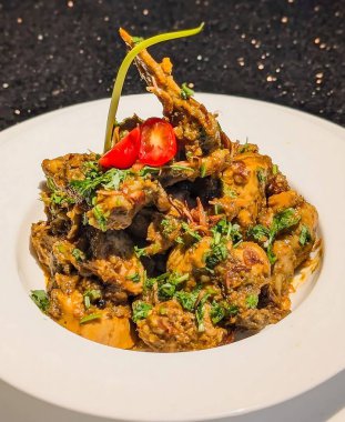 Bir kase bol baharatlı et körisi kalın kırmızımsı kahverengi soslu, doğranmış otlar, kırmızı biber dilimleri ve yeşil bir biber sapıyla süslenmiş..