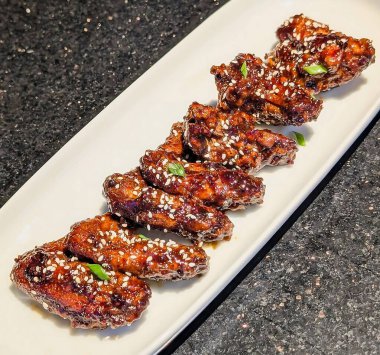 Koyu, parlak bir sosla kaplanmış bir sıra jöleli tavuk kanadı beyaz dikdörtgen bir tabakta düzgünce düzenlenir..