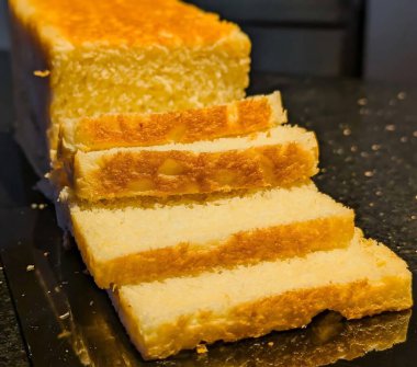 Kısmen dilimlenmiş beyaz ekmek, altın kabuklu ve içi yumuşak, siyah bir yüzeye yerleştirilmiş.