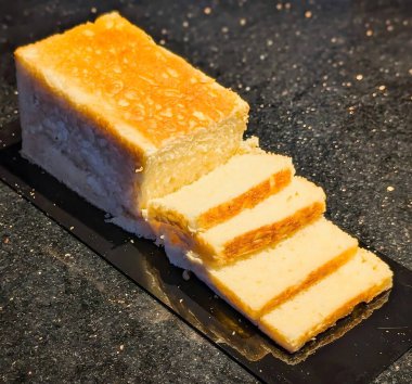 Kısmen dilimlenmiş beyaz ekmek, altın kabuklu ve içi yumuşak, siyah bir yüzeye yerleştirilmiş.