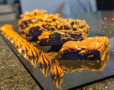 Gourmet çikolatalı brownie dilimleri yoğun şekerli bir ortası ve çatırtılı üstü parlak, siyah servis tabağı üzerine yerleştirilmiş, aksanlı çikolata kremalı..