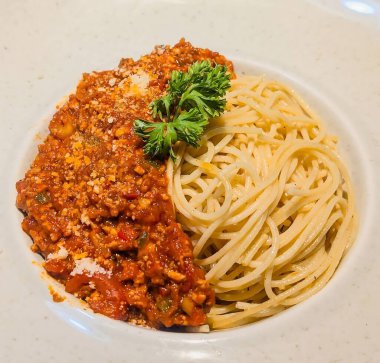 Klasik bir spagetti tabağı, taze maydanozla süslenmiş ve rendelenmiş peynirli domates sosuyla servis edilir.