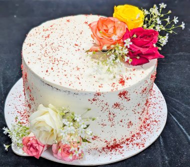 Zarif bir kutlama pastası, pürüzsüz beyaz kremayla kaplı ve canlı taze güller ve dolgu çiçeklerle süslenmiş..