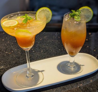 Zarif kadehlerle servis edilen turunçgil kokteylleri, canlı renklerle kaplı ve limon dilimleri ve taze nane ile süslenmiş..