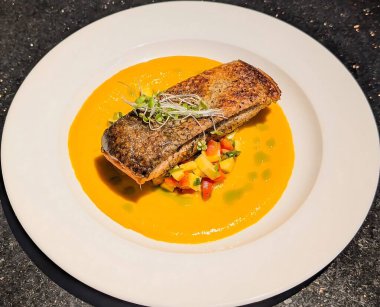 Kıtır derili kurutulmuş somon balığı turuncu biberli ve yeşil yağ damlacıklarıyla süslenmiş canlı bir sebze ve meyve yatağının üzerinde servis edilir..