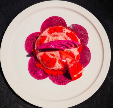 Kırmızı ve beyaz kıvrımlı donmuş mus ya da dondurma içeren sanatsal bir tatlı. Çiçek deseninde ejderha meyve dilimleri var.