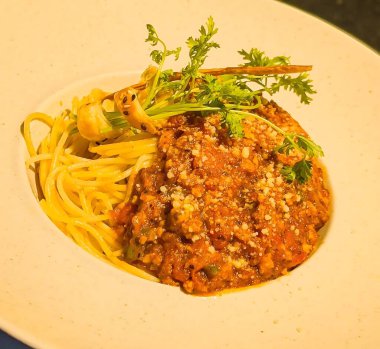 Klasik bir spagetti tabağı, taze maydanozla süslenmiş ve rendelenmiş peynirli domates sosuyla servis edilir.