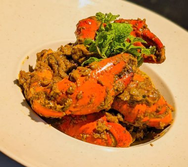 Vibrant crab curry featuring large claws coated in rich, aromatic sauce, garnished with fresh mint leaves.