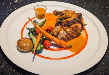 Işıl ışıl portakal soslu ızgara tavuk yanında bebek havuç, vişneli domates, brokoli ve bir bardak ekstra sosla birlikte beyaz tabakta küçük bir rulo..