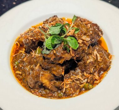 Baharatlı hindistan cevizi sosunda yavaş pişirilmiş sığır eti, kızarmış soğan ve taze nane ile süslenmiş yeşil biber..