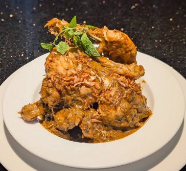 Işıltılı kahverengi sosla kaplanmış baharatlı tavuk üzerine kızarmış soğan ve taze nane, rafine edilmiş bir sunum için beyaz bir tabakta kaplanmış..