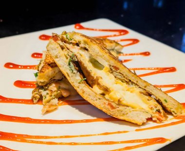 Lezzetli bir tost sandviçi. Erimiş peynir katmanları ve beyaz bir tabakta taze otlar. Artistik kırmızı sos serpiştirilmiş..