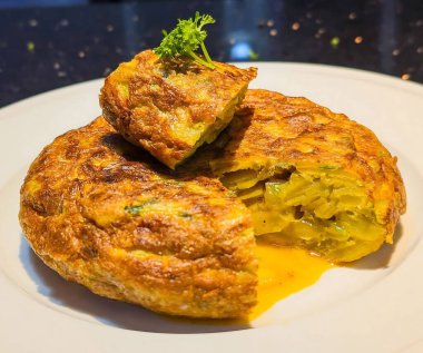 Beyaz bir tabakta servis edilen klasik İspanyol tortilla de patatas, altın-kahverengi bir kabuk ve mükemmel bir püre ve yumurta merkezi içerir..