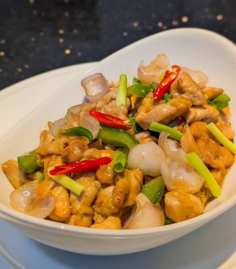 Beyaz bir kasede servis edilen baharatlı kırmızı biberli ve kıtır soğanlı Asya usulü kızarmış tavuk..