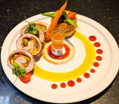 Sebzelerle doldurulmuş gurme eti katmanlı sebze pastası ve beyaz bir tabakta küçük bir bardak altın sosla kaplanır..