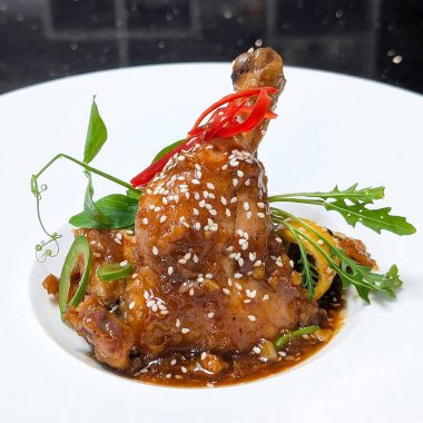 Susam tohumlu jöleli tavuk budu, dilimlenmiş kırmızı biber ve taze bitkiler, beyaz bir tabakta yapraklı yeşilliklerle servis edilir..