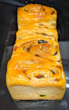 Meyve ve cevizli tatlı ekmek. Kuru üzümlü ve şekerli meyveli somun. Parlak bir altın kaplamayla kaplanır ve siyah bir arka planda beyaz tabakta servis edilir..