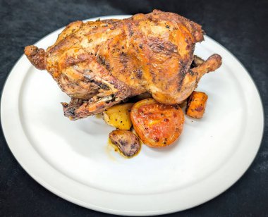 Kızarmış bütün tavuk baharatlı ve yanında fırında domates, mantar, patates ve havuç ile servis ediliyor..