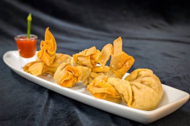 Canlı kırmızı biber soslu kızarmış wonton, yeşil saplı ve susamlı, çıtır çıtır ve aromalı..