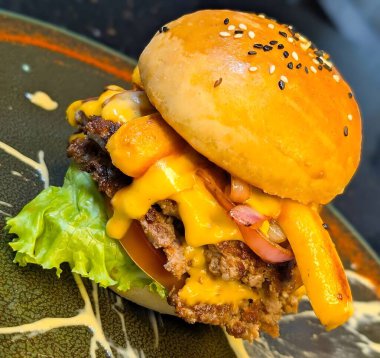 İki etli çizburgerli gurme, erimiş çedar peyniri, ızgara soğan, kıvırcık patates kızartması ve sanatsal sos ile servis edilen marul ve domates..